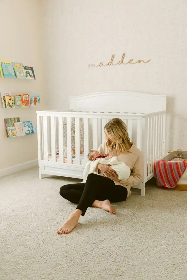 Tired mother holding baby beside crib at night